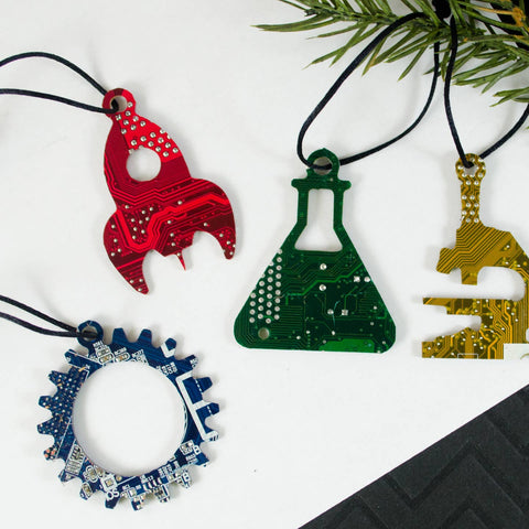 Four unique Christmas ornaments made from circuit boards on a white background with greenery.