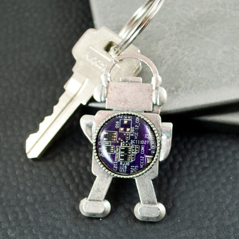 Keychain with robot design featuring a purple circuit board on a gray surface.