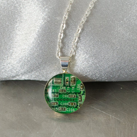Necklace with a green circuit board pendant on a metallic surface