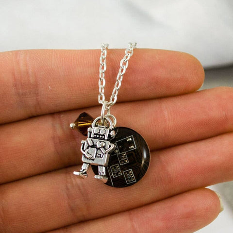 Necklace with a robot charm held between fingers on a white background