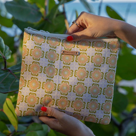 Hand holding a patterned pouch with a brand name against a green leafy background