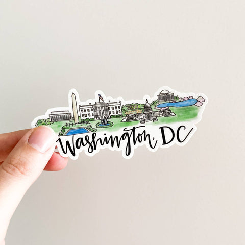 Sticker of Washington, DC with a hand holding it on a light gray background