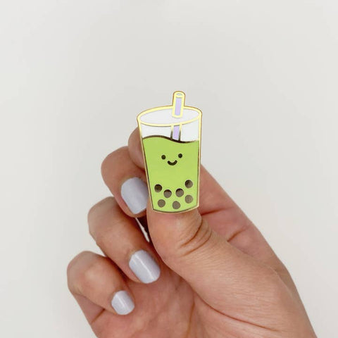 Hand holding a green bubble tea-shaped pin against a white background