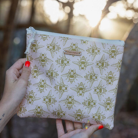 Hand holding a pouch with bee pattern against a blurred natural background