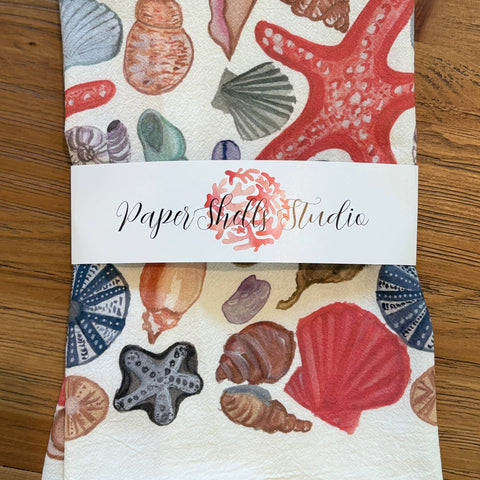 Set of three paper napkins with seashell and starfish patterns on a wooden surface.