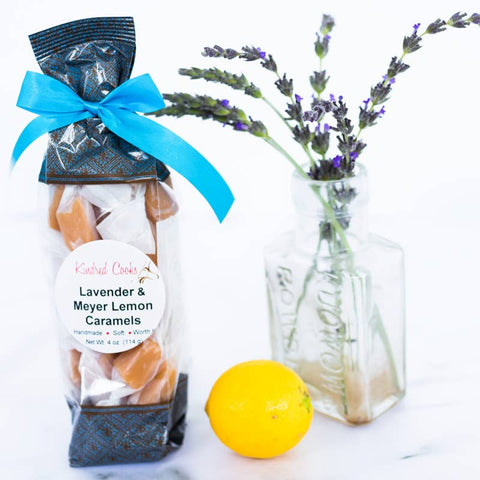 Packaged lavender and meyer lemon caramels with a blue ribbon, lemon, and vase of lavender on a white background.