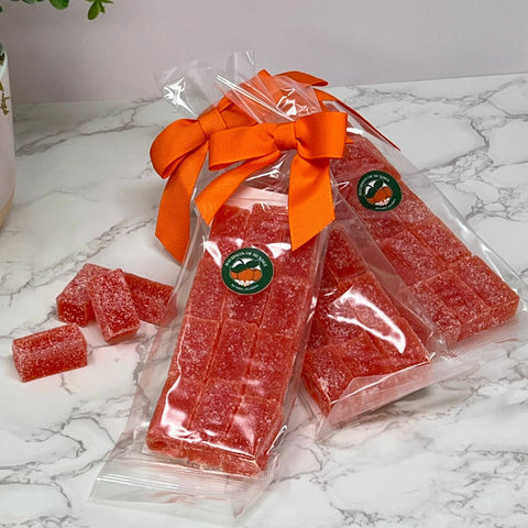 Packaged red gummy treats with an orange bow on a marble surface.