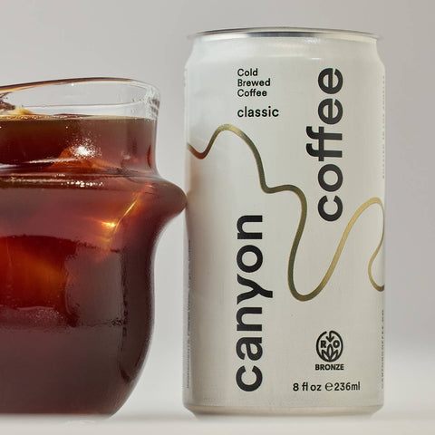 Canyon Cold Brewed Coffee can next to a glass of iced coffee on a light background