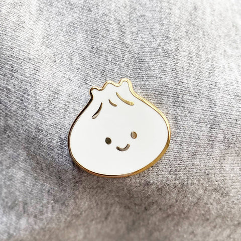 Pin with a cartoonish dumpling design on a textured gray background