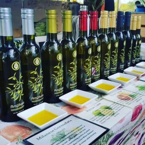 A table displaying various bottles of infused olive oil, with small plates of oil in front of each bottle. The bottles are labeled with different flavors such as Herbs de Provence and Persian Lime.