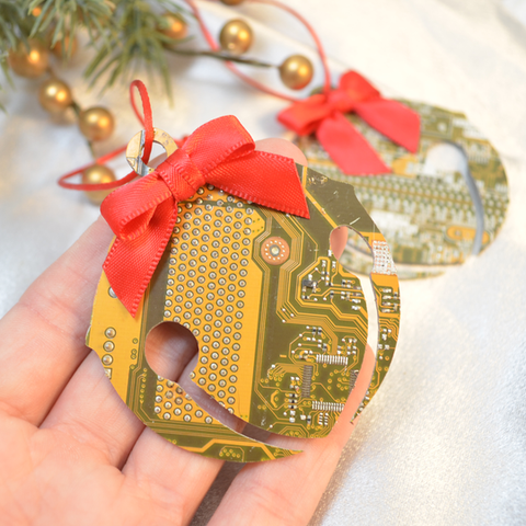 Hand holding a Christmas ornament made from a circuit board with a red bow, surrounded by festive decorations.