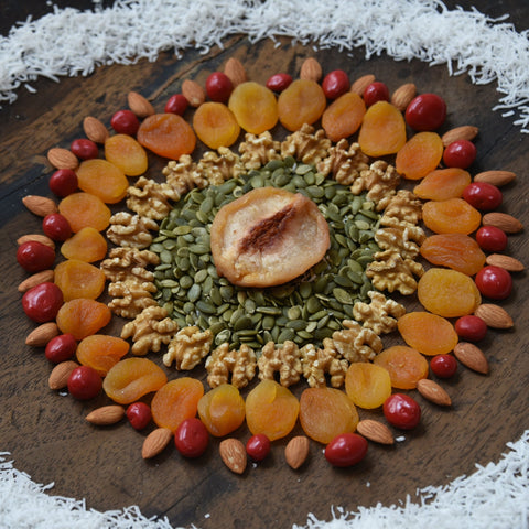 Decorative arrangement of dried fruits and nuts on a wooden board with coconut flakes around.