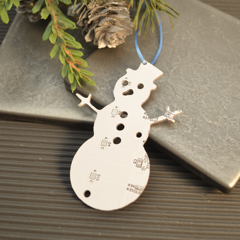 Metal snowman ornament with circuit board design on a textured surface with greenery.