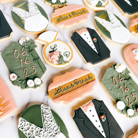 Decorative cookies shaped like wedding attire and elements on a white surface