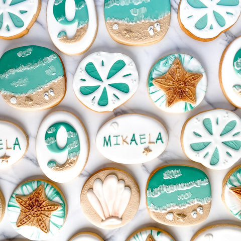 Decorative cookies with beach-themed designs and the name 'MIKAELA'.