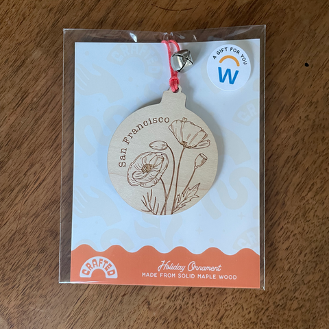 Wooden ornament with floral design on a clear card with a Woodbury logo.