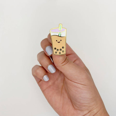 Hand holding a cute cartoon-style boba tea pin against a plain background