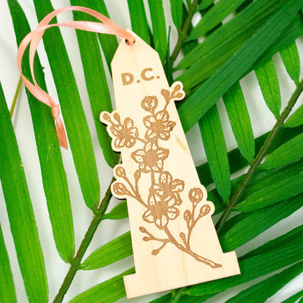 Decorative wooden tag with floral design and 'D.C.' text on a green leaf background