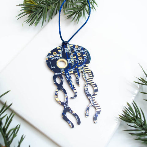 Jellyfish-shaped ornament made from blue circuit board material, hanging on a branch.