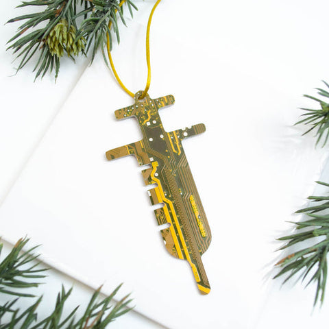 Decorative key-shaped ornament made from circuit board material, hanging on a string with greenery around.