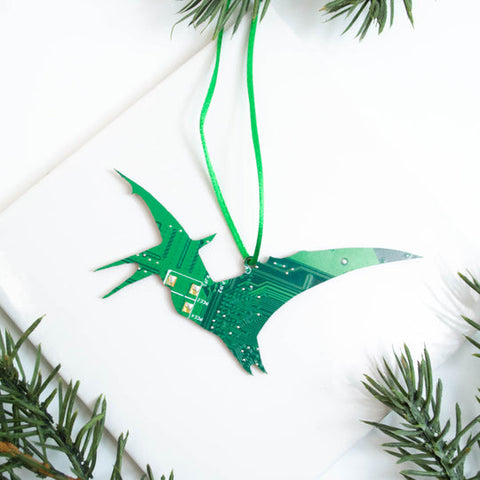 Green electronic circuit board ornament shaped like a dinosaur on a white background with greenery.