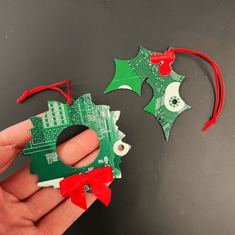 Hand holding a green circuit board Christmas ornament with red ribbons on a black background