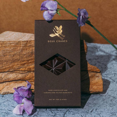 Chocolate bar packaging with 'Deux Cranes' branding on a textured surface with purple flowers.