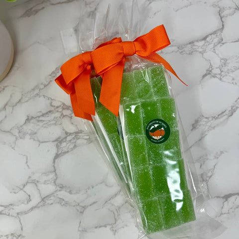 Green gummy bears in clear packaging with an orange bow on a marble surface