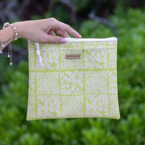 Hand holding a green patterned pouch against a blurred green background