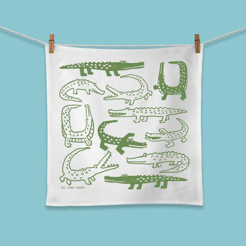 White towel with green crocodile illustrations hanging on a line against a blue background
