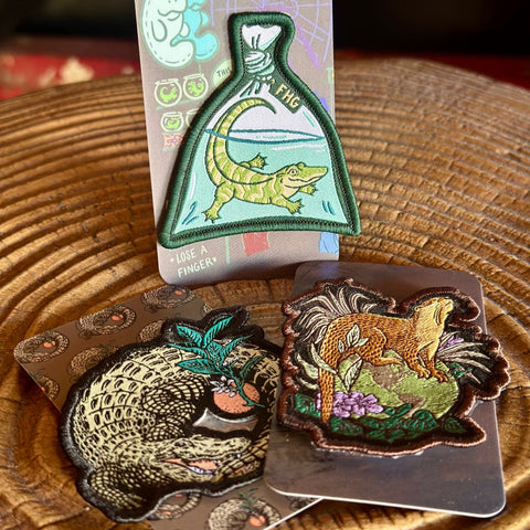 Three embroidered patches on a wooden surface with a dark background