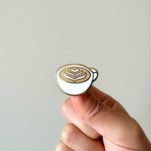 Pin with a cappuccino design held by a hand against a plain background