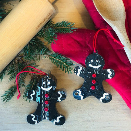 Two gingerbread man ornaments on a wooden surface with greenery and a red cloth.