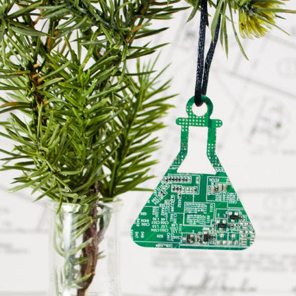 Green electronic circuit board ornament shaped like a beaker hanging on a Christmas tree.