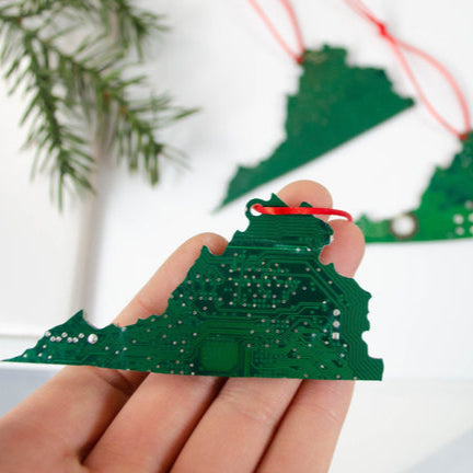 Hand holding a green electronic circuit board ornament with more ornaments in the background.