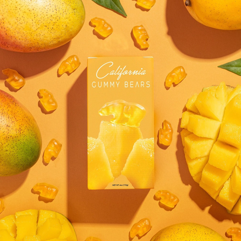 Box of California Gummy Bears surrounded by gummy bears and mangoes on a yellow background