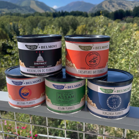 Five cans of Belmont Peanuts stacked on a metal railing with a scenic background
