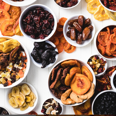 Assorted dried fruits in small white bowls on a light wooden surface