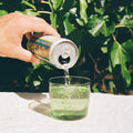 Hand pouring a can of Peroni into a glass with greenery in the background
