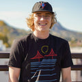 Person wearing a black t-shirt with a graphic design, sitting on a wooden bench outdoors.