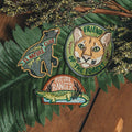 Three embroidered patches on a wooden surface with green leaves