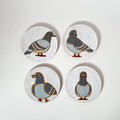 Four ceramic coasters with pigeon design on a white surface
