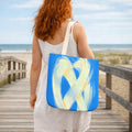 Woman with a blue tote bag featuring a yellow abstract design, standing on a wooden boardwalk by the beach.