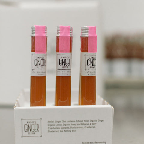 Three bottles of Annie's Ginger Elixir with pink caps on a white box labeled 'SHOTS!'.