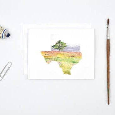 A watercolor art print of Texas showing a tree in a field, displayed on a white background with a paint tube, paperclip, and paintbrush nearby.