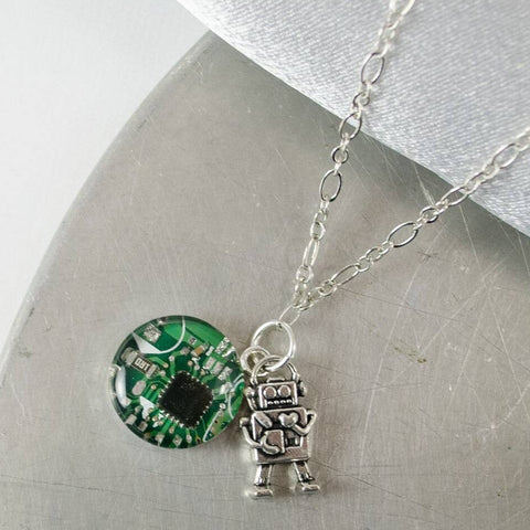 Necklace with a green circuit board eye and robot charm on a metallic surface.