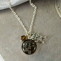 Necklace with a round pendant and a small square charm on a textured surface