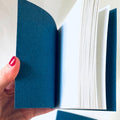 Hand holding a blue notebook open to show pages, with another notebook in the background.