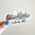 St. Louis, MO sticker held by a hand on a light gray background
