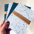 Hand holding a stack of notebooks made with recycled denim bits
